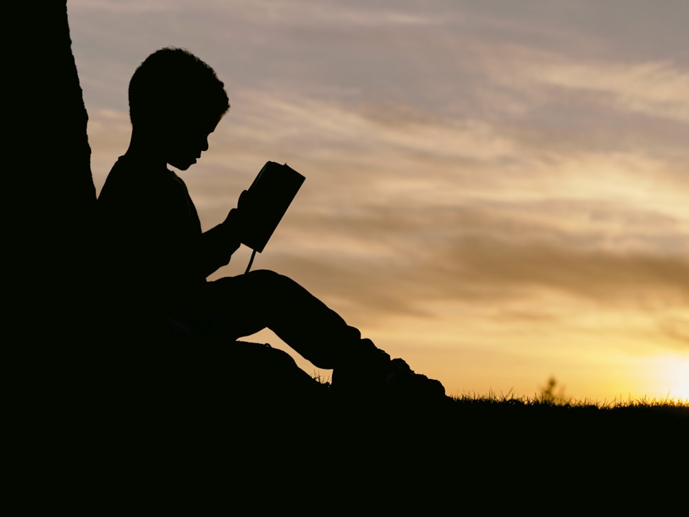 Silhouette eines Kindes, das während des Sonnenuntergangs hinter einem Baum sitzt