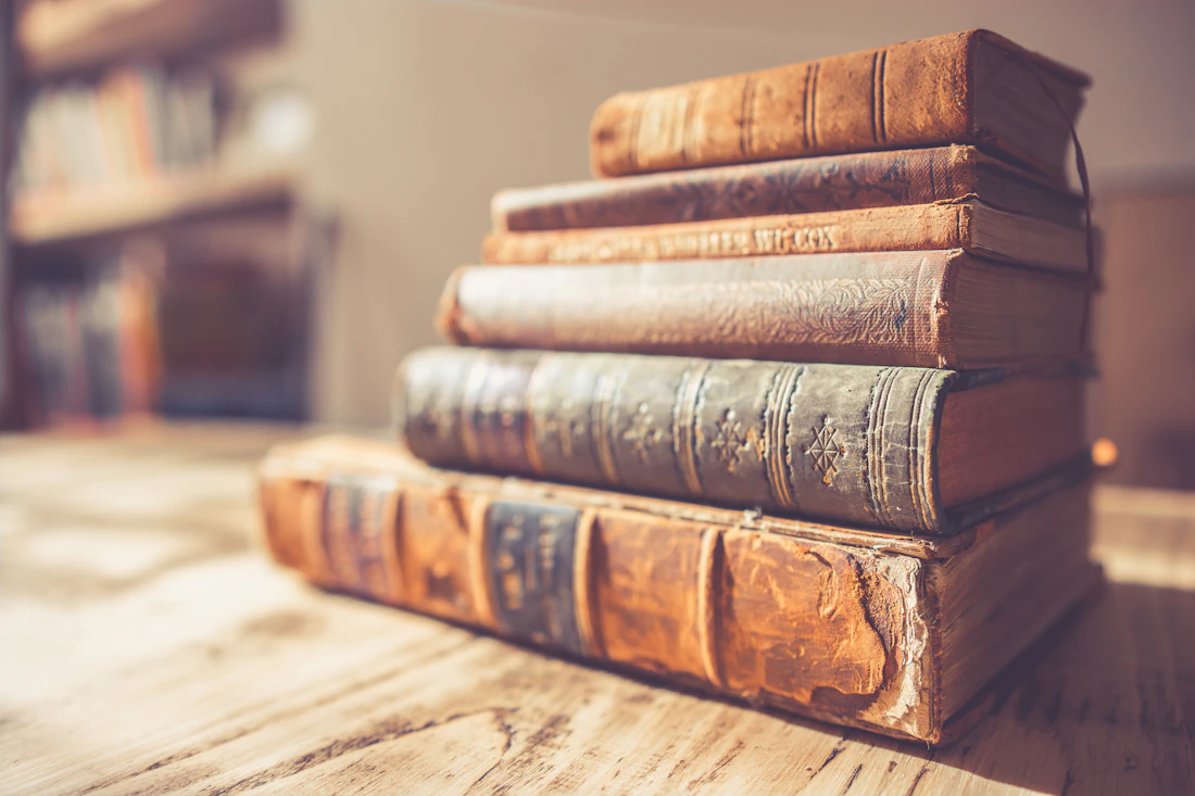 Stapel antiquarischer Bücher mit geprägten Rücken vor unscharfem Regal in warmem Licht
