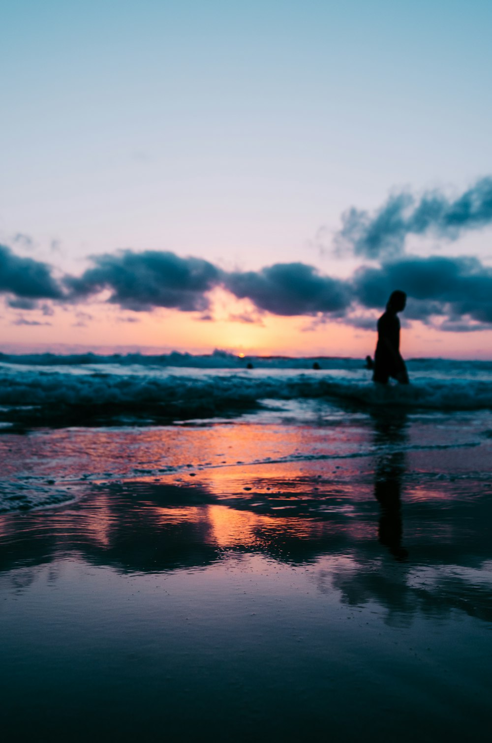 골든 아워 동안 흐린 하늘 아래 해변을 걷는 사람의 실루엣 사진