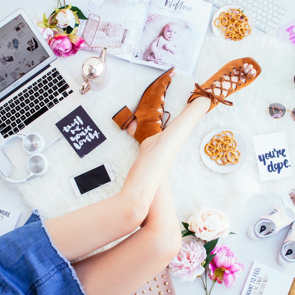 woman wearing brown open-toe chunky sandals sitting beside white smartphone, headphones and laptop