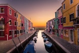 blue boats parked on river between multicolored buildings at sunset