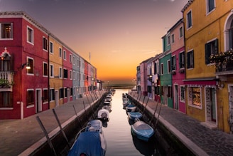 blue boats parked on river between multicolored buildings at sunset