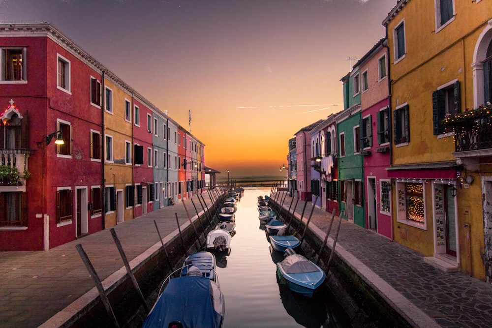 Bateaux bleus garés sur la rivière entre des bâtiments multicolores au coucher du soleil