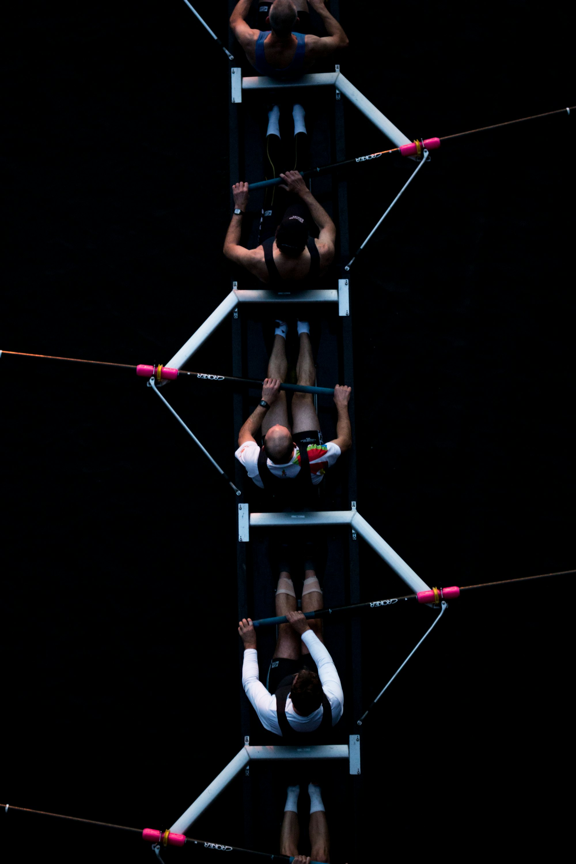 An overhead view of a rowing team, showing five people, each rowing through the water.