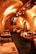 The image depicts an elegant restaurant interior with a vaulted brick ceiling and warm lighting. The tables are set with white tablecloths, red napkins, glassware, and cutlery, creating a cozy and inviting atmosphere. The seating consists of wooden chairs, and the room has an arched architecture feature, adding to the charm.