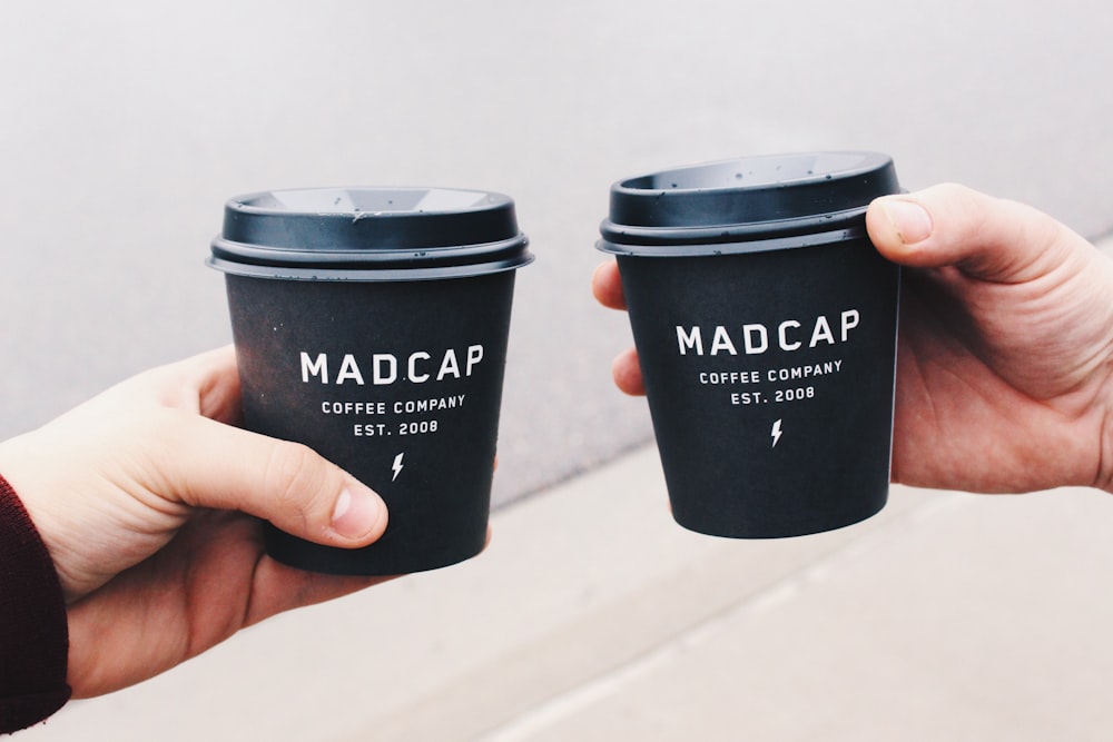 two person holding black Madcap coffee disposable cups