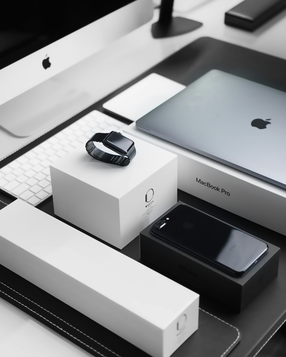 Space Black Case Apple Watch, silbernes MacBook Pro, tiefschwarzes iPhone 7 Plus und silberner iMac mit entsprechenden Boxen