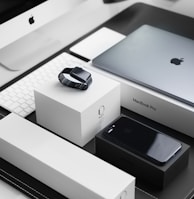 space black case Apple Watch, silver MacBook Pro, jet black iPhone 7 Plus, and silver iMac with corresponding boxes