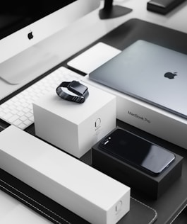 space black case Apple Watch, silver MacBook Pro, jet black iPhone 7 Plus, and silver iMac with corresponding boxes