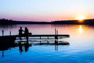 A serene moment of a couple looking out over a calm lake at sunset, reflecting on their path.