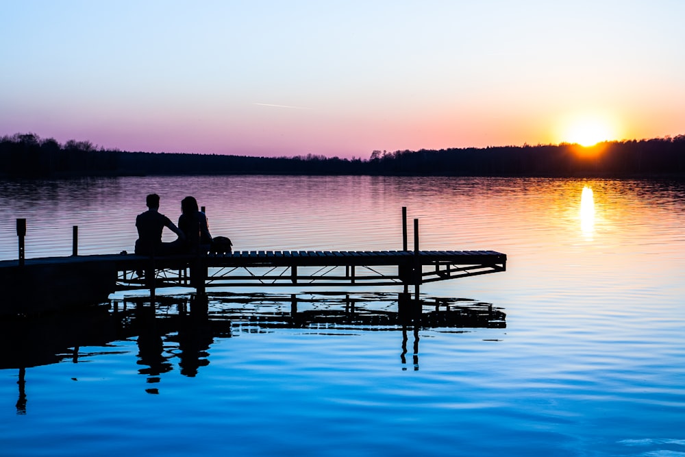 silhouette of two persons sitting on dock