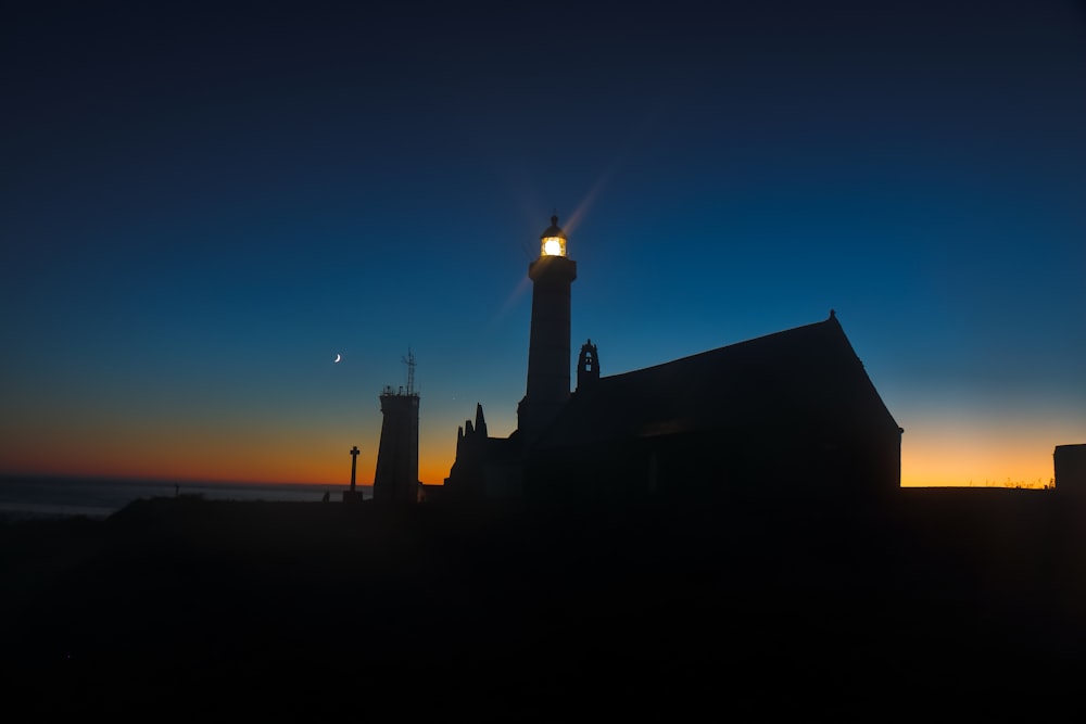 オレンジ色の夕暮れ時の灯台のシルエット