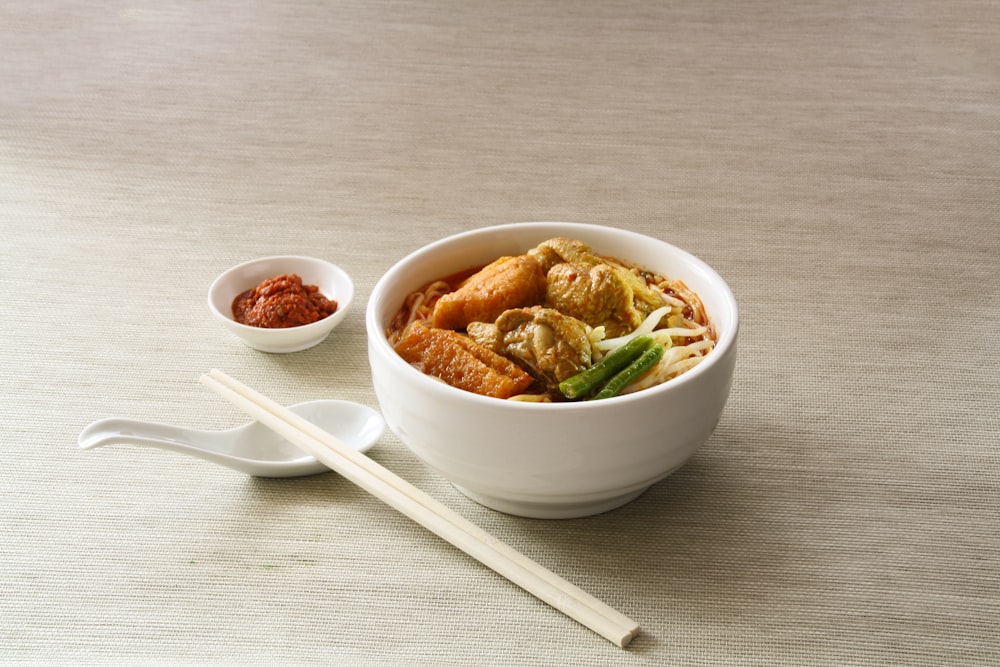 white ceramic bowl filled with cooked noodles near white chopsticks