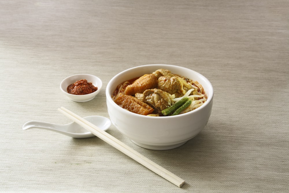 white ceramic bowl filled with cooked noodles near white chopsticks