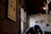 A framed picture with the word 'SANITY' hangs on a brick wall. A person with their head bowed is seen in the background wearing a checkered shirt. The room has rustic decor, with exposed wooden beams and soft lighting creating a dim atmosphere.