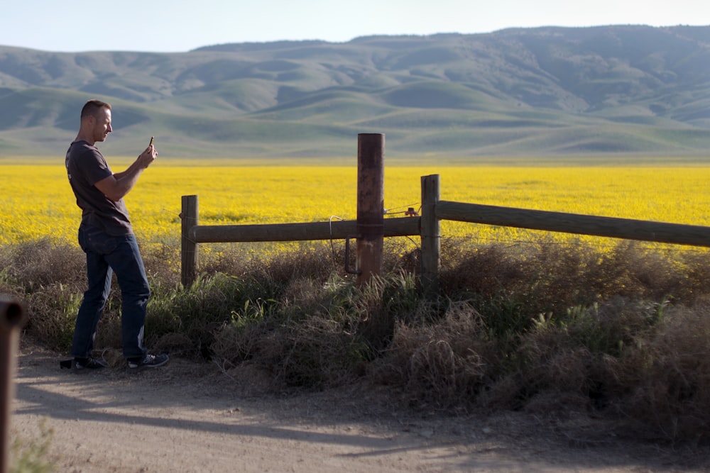 man using smartphone standing beside fence