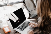 girl wearing grey long-sleeved shirt using MacBook Pro on brown wooden table