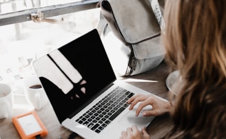 girl wearing grey long-sleeved shirt using MacBook Pro on brown wooden table