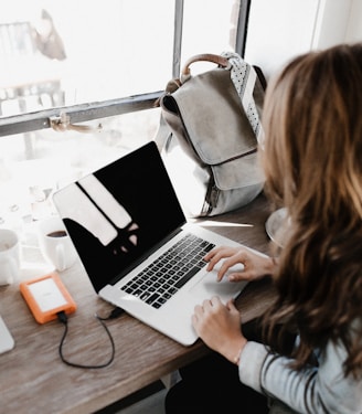 girl wearing grey long-sleeved shirt using MacBook Pro on brown wooden table