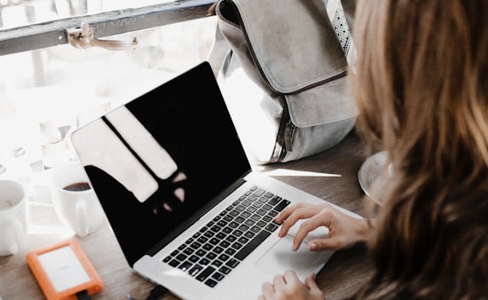 girl wearing grey long-sleeved shirt using MacBook Pro on brown wooden table