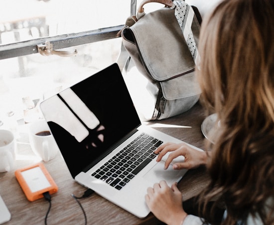 girl wearing grey long-sleeved shirt using MacBook Pro on brown wooden table