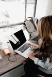 girl wearing grey long-sleeved shirt using MacBook Pro on brown wooden table