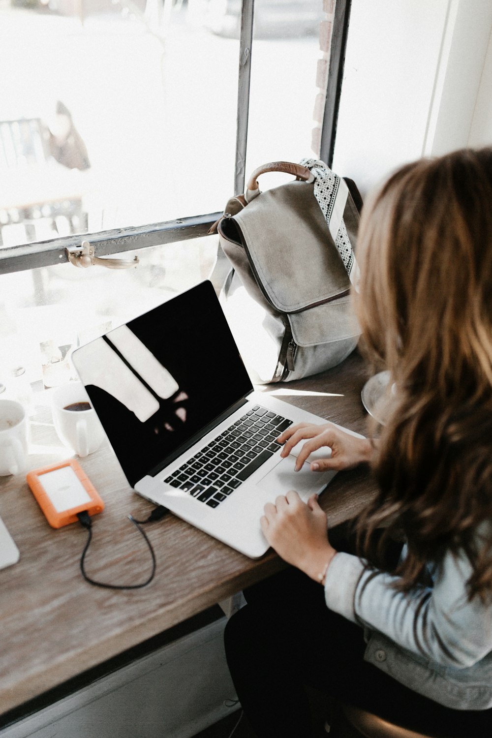 fille portant une chemise grise à manches longues à l’aide d’un MacBook Pro sur une table en bois marron