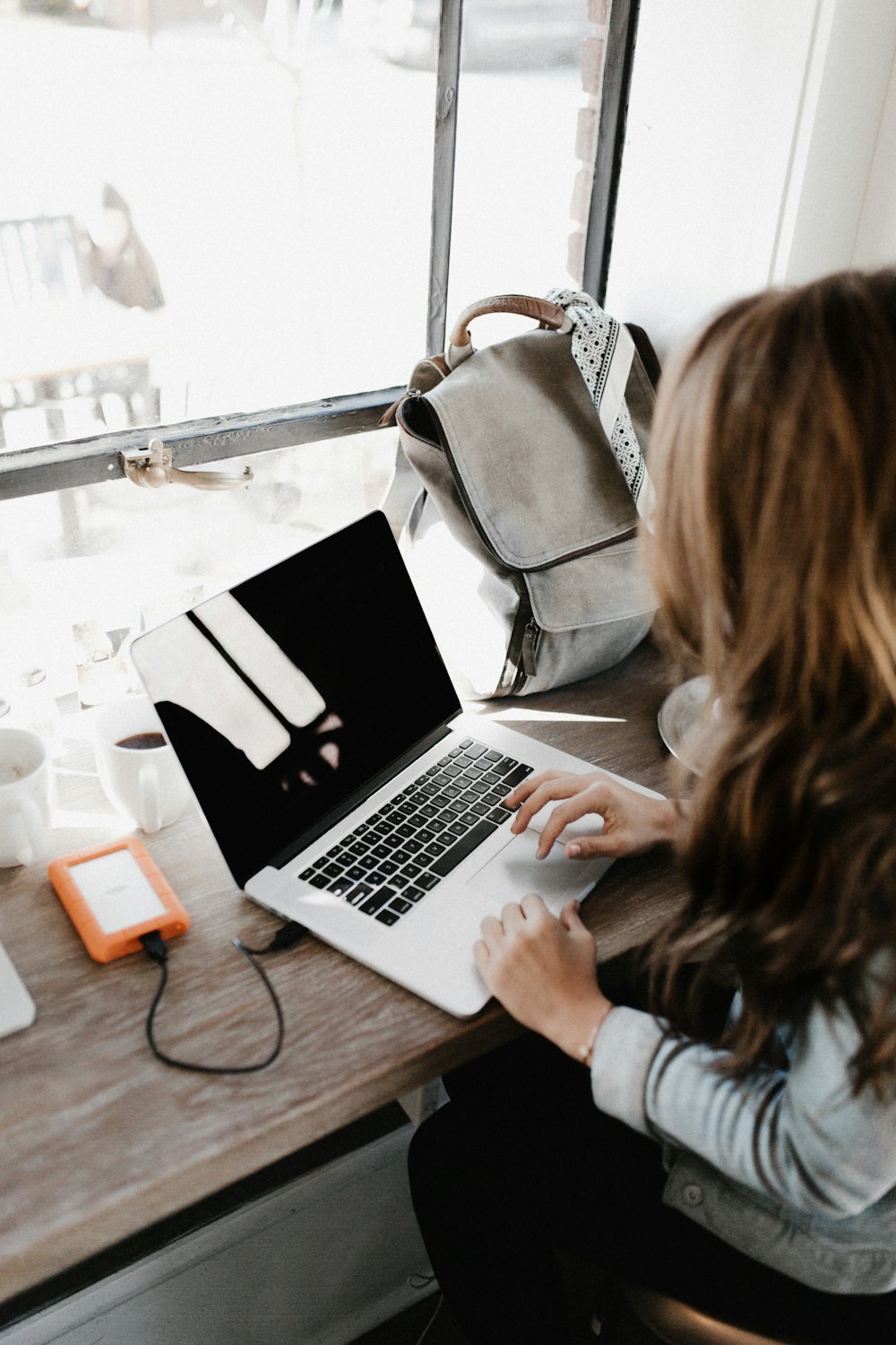 灰色の長袖シャツを着て、茶色の木製のテーブルでMacBook Proを使う女の子