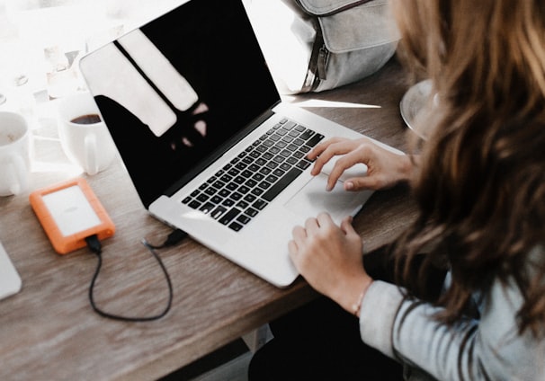 girl wearing grey long-sleeved shirt using MacBook Pro on brown wooden table