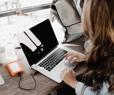 girl wearing grey long-sleeved shirt using MacBook Pro on brown wooden table