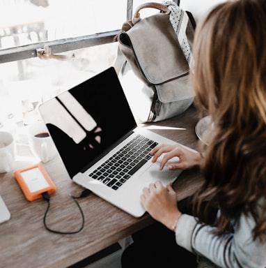 girl wearing grey long-sleeved shirt using MacBook Pro on brown wooden table