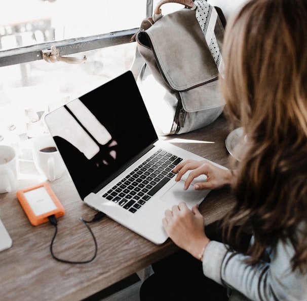 girl wearing grey long-sleeved shirt using MacBook Pro on brown wooden table