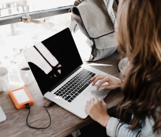 girl wearing grey long-sleeved shirt using MacBook Pro on brown wooden table