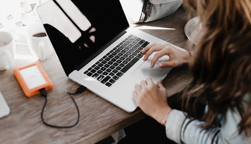 girl wearing grey long-sleeved shirt using MacBook Pro on brown wooden table