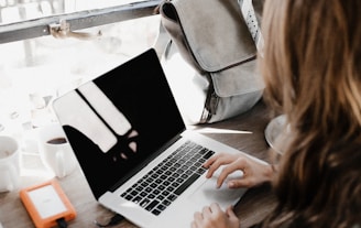 girl wearing grey long-sleeved shirt using MacBook Pro on brown wooden table