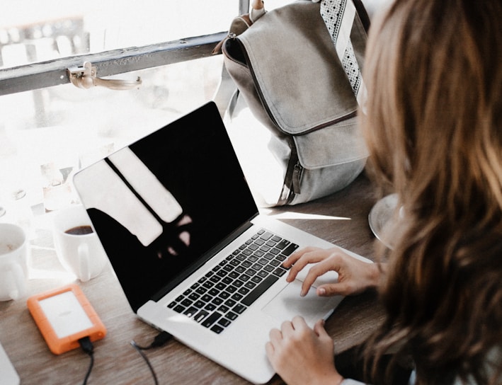 girl wearing grey long-sleeved shirt using MacBook Pro on brown wooden table