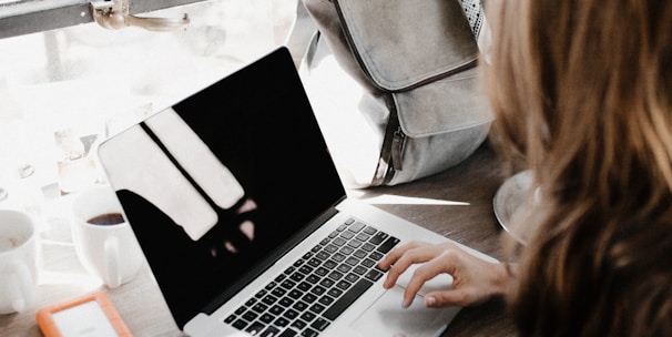 girl wearing grey long-sleeved shirt using MacBook Pro on brown wooden table