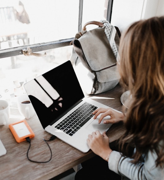 girl wearing grey long-sleeved shirt using MacBook Pro on brown wooden table