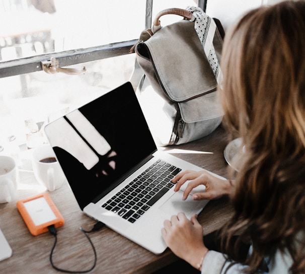 girl wearing grey long-sleeved shirt using MacBook Pro on brown wooden table