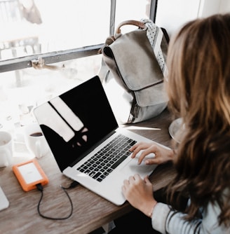 girl wearing grey long-sleeved shirt using MacBook Pro on brown wooden table