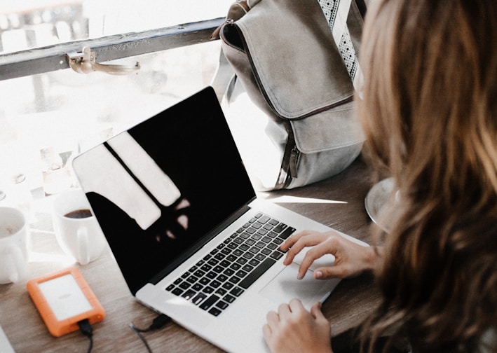 girl wearing grey long-sleeved shirt using MacBook Pro on brown wooden table