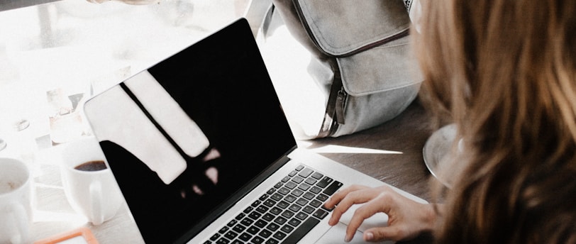 girl wearing grey long-sleeved shirt using MacBook Pro on brown wooden table