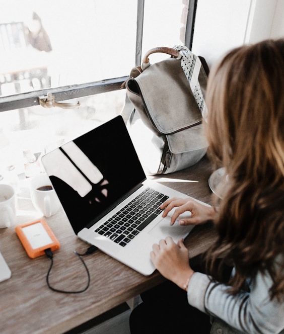 girl wearing grey long-sleeved shirt using MacBook Pro on brown wooden table