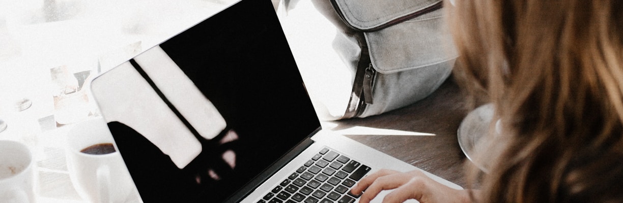 girl wearing grey long-sleeved shirt using MacBook Pro on brown wooden table