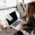 girl wearing grey long-sleeved shirt using MacBook Pro on brown wooden table