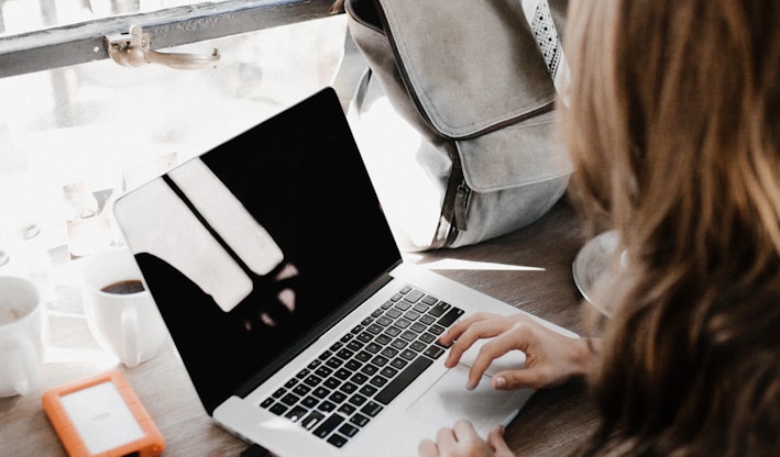 girl wearing grey long-sleeved shirt using MacBook Pro on brown wooden table