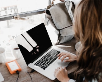 girl wearing grey long-sleeved shirt using MacBook Pro on brown wooden table