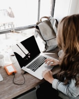 girl wearing grey long-sleeved shirt using MacBook Pro on brown wooden table