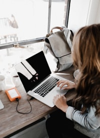 girl wearing grey long-sleeved shirt using MacBook Pro on brown wooden table