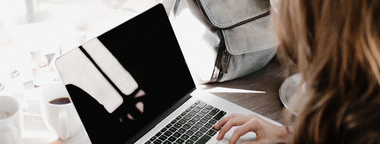 girl wearing grey long-sleeved shirt using MacBook Pro on brown wooden table